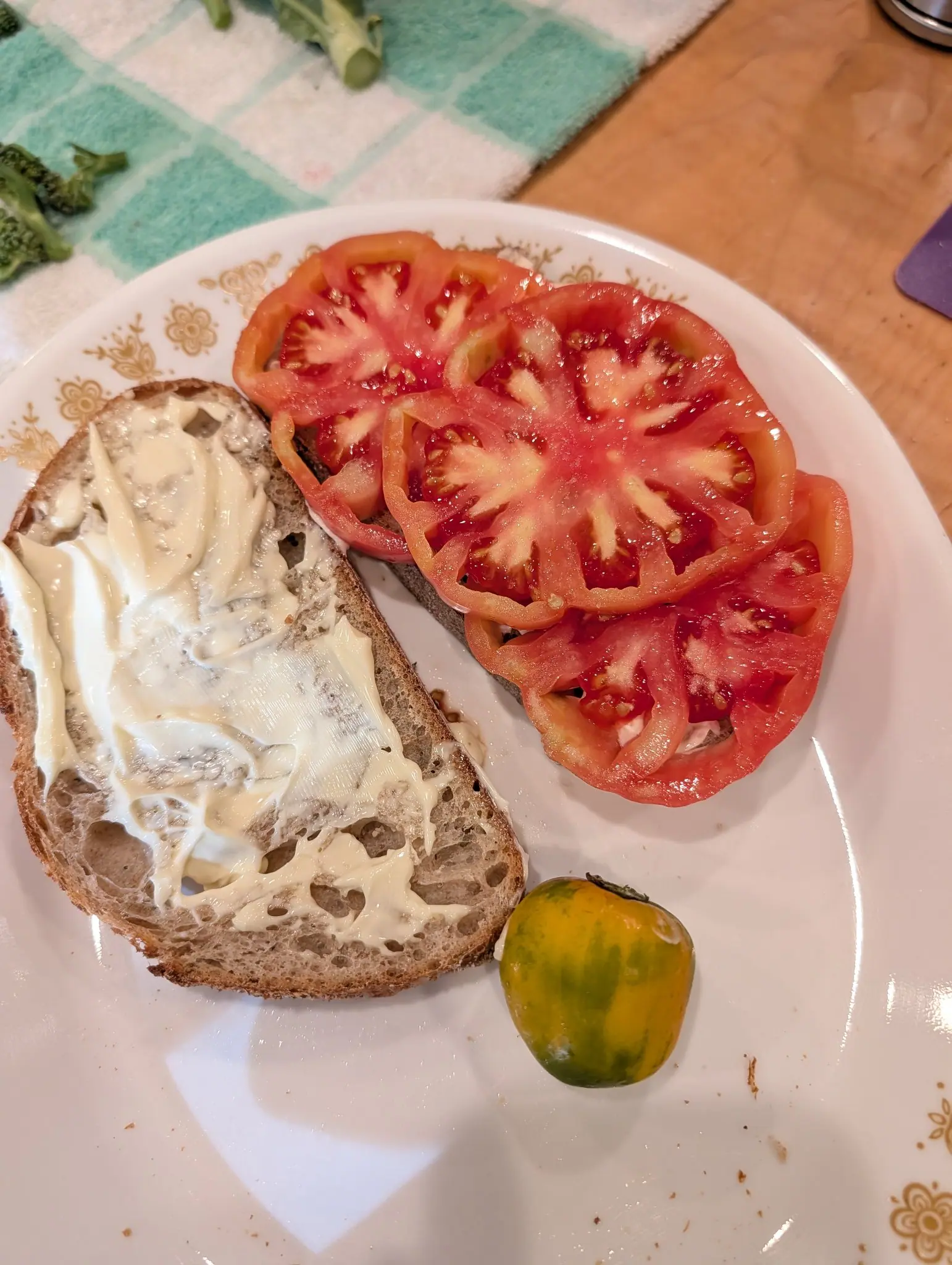 Lunch half built on 16 August: four thick slices shingled across a slab of open-crumbed bread, wide enough to overhang it, deep pink-red at the rim and paling to cream at the core. A small one striped yellow-gold and green stands on its shoulder in front.