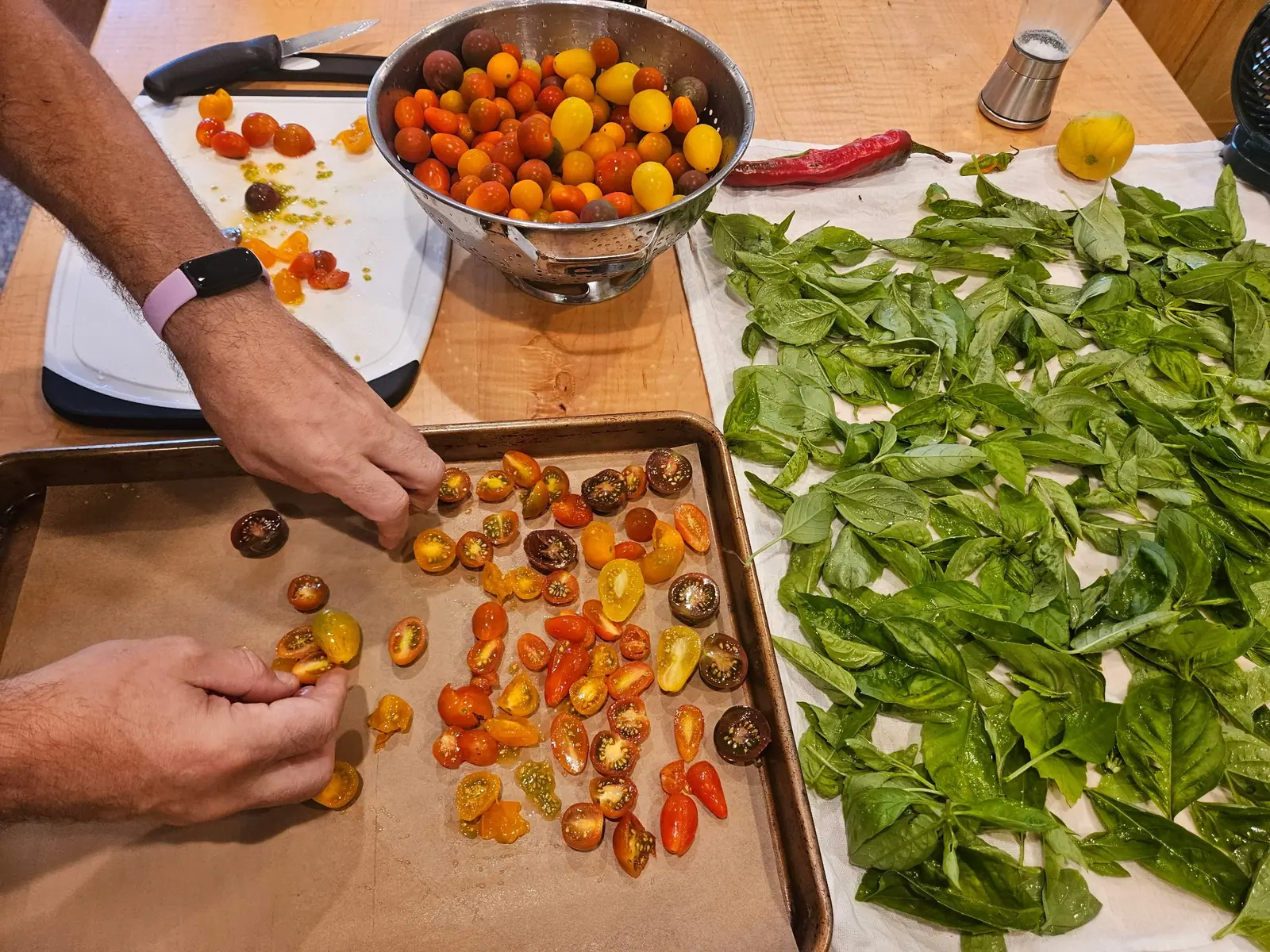 Halved fruit laid cut-side up on a parchment-lined sheet pan on 17 September, scarlet, gold and dark purple-brown faces glossy with oil, their pale green gel and seeds showing; washed whole ones wait in a steel colander under even indoor light.