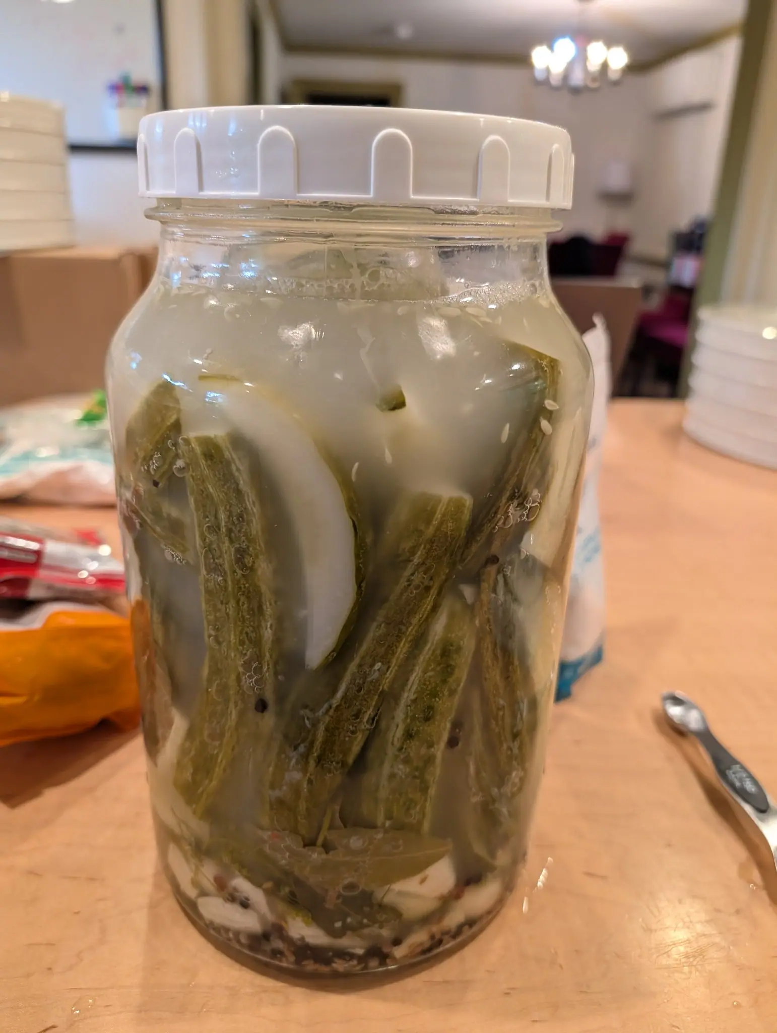 A jar put up on 3 August, eight ridged green pods wedged upright and crossing one another in cloudy brine with a bay leaf lying flat on the bottom beneath them, and the one cut square across shows a hollow dark cavity inside rather than solid flesh.
